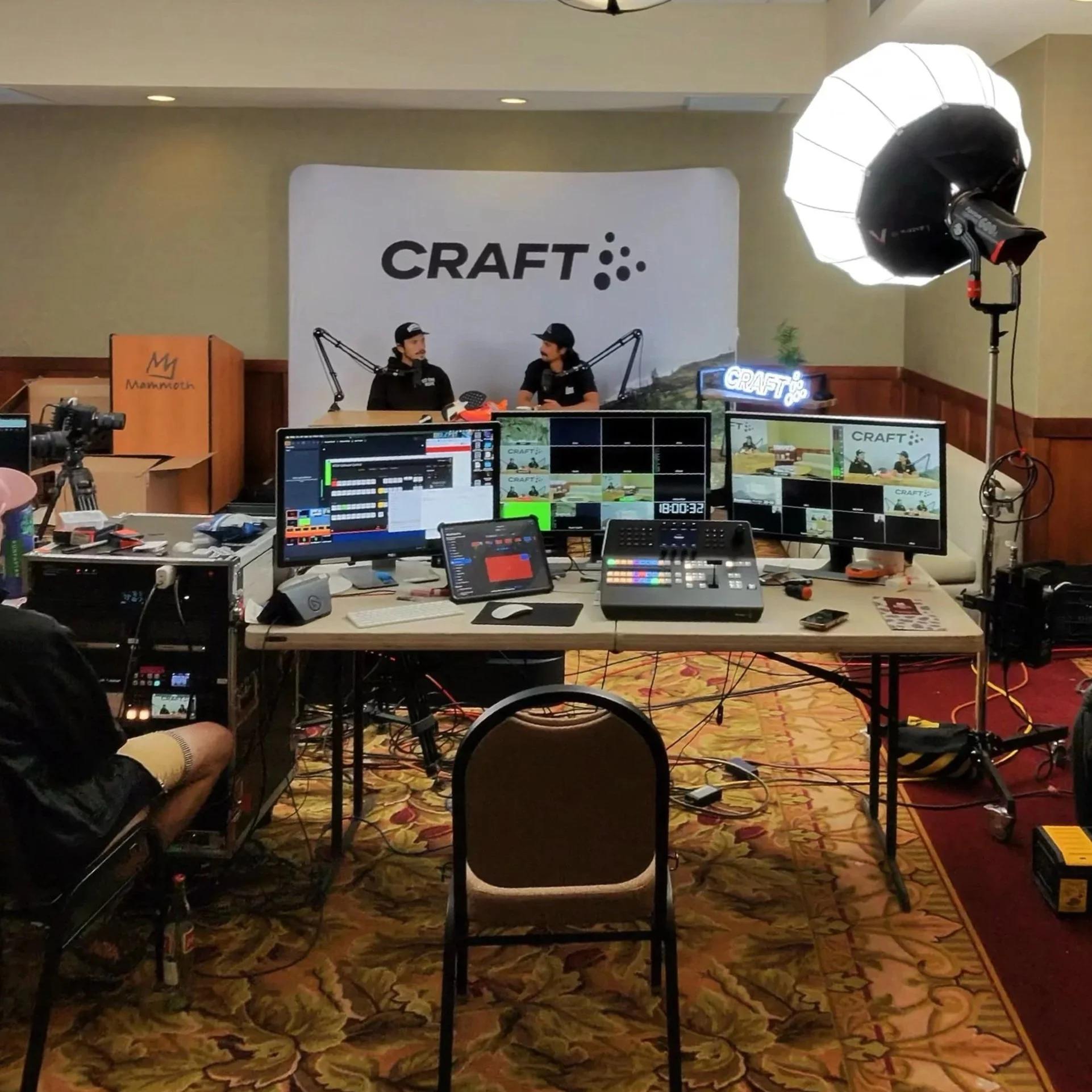 A field production desk with a switcher, multiview monitors and two hosts on set